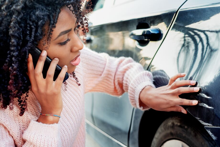 Frau sitzt vor ihrem Unfallauto und telefoniert