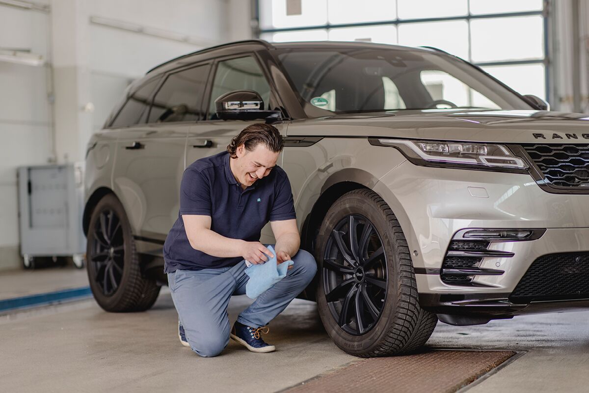 Mitarbeiter kniet lachend vor Land Rover mit einem Tuch in der Hand