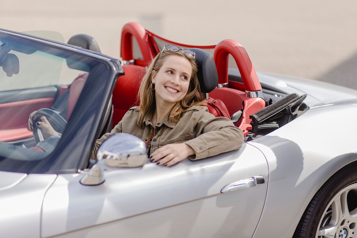 Lächelnde Frau sitzt in einem Auto und fährt zur HU Hauptuntersuchung in Köln